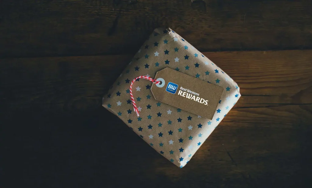 Pictured is a square gift package with paper decorated with blue and light blue stars, to which is attached a label with the best western rewards logo
