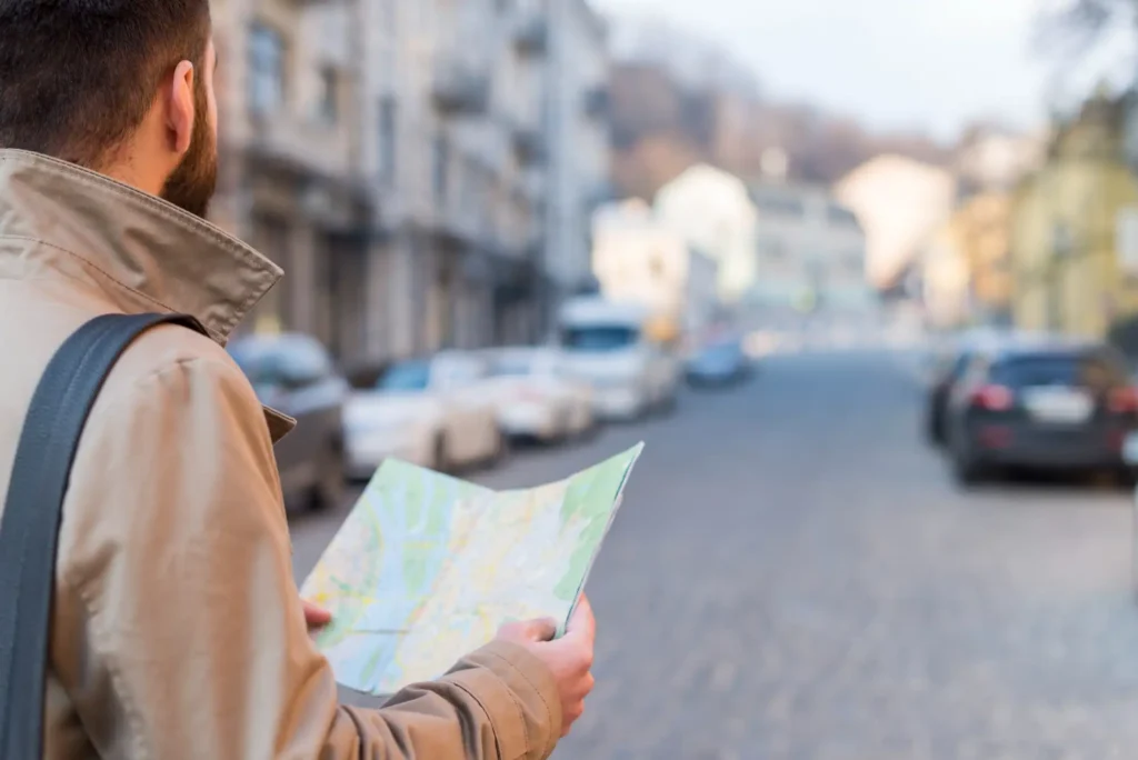 The image shows a schiema man holding a map of the city and, in the background, a street along which cars are parked