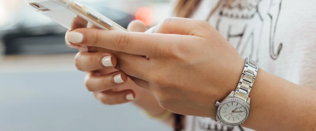A close-up of two women's hands using a smartphone. A steel watch is visible in the image on the left wrist