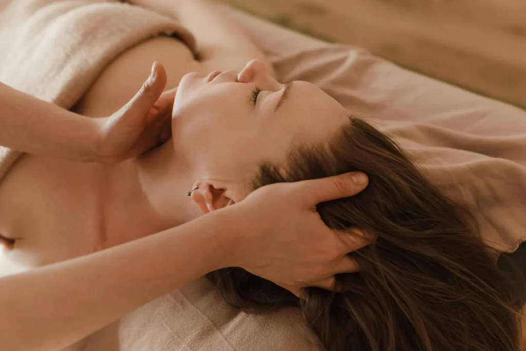 Pictured is a close-up of a woman lying on a massage table as two hands massage her neck